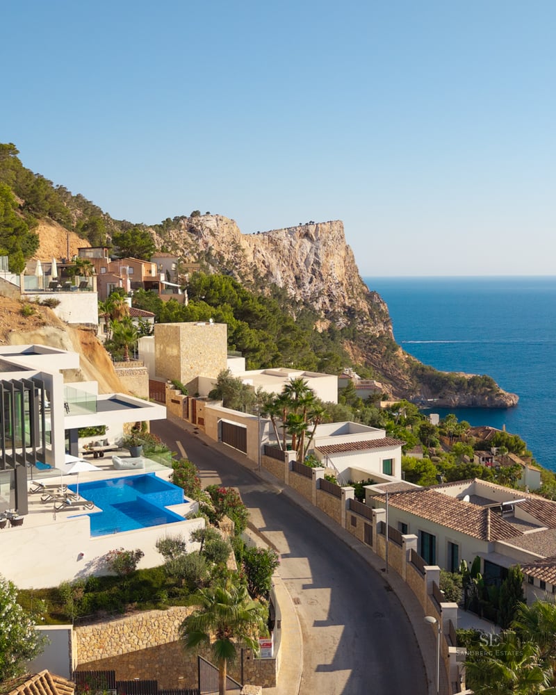 Aerial view of a white modern villa with an infinity pool on a cliffside overlooking the blue Mediterranean sea.