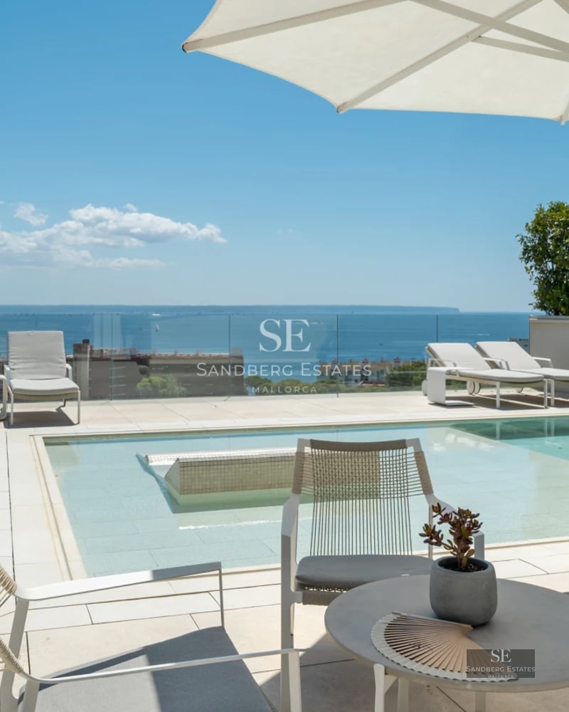 Spacious balcony with panoramic sea views. Glass railing, wooden floor, modern outdoor furniture. Soft lighting and relaxing atmosphere.