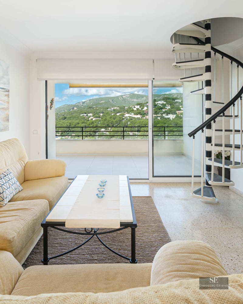 Bright living room featuring a cream sofa, black and white spiral staircase, and balcony with mountain views.