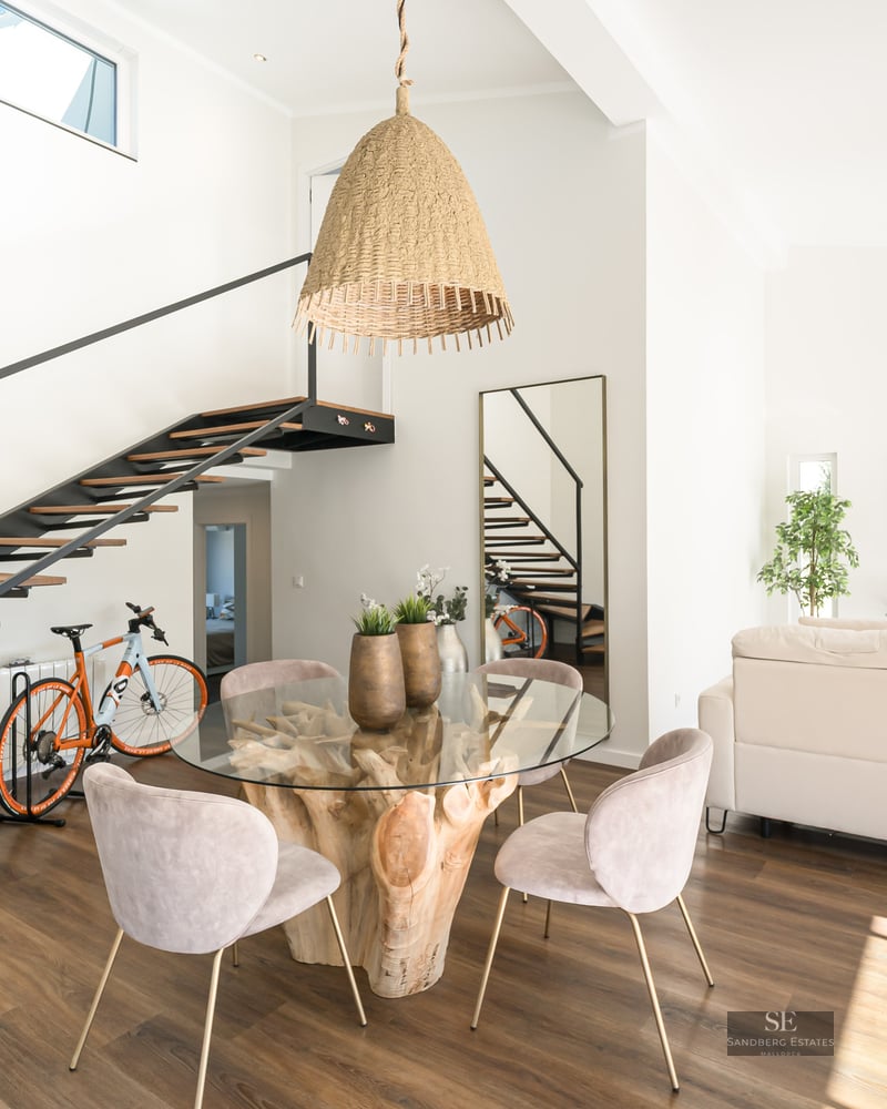 Salon lumineux à aire ouverte avec table en bois flotté, chaises en velours et escalier flottant en bois.