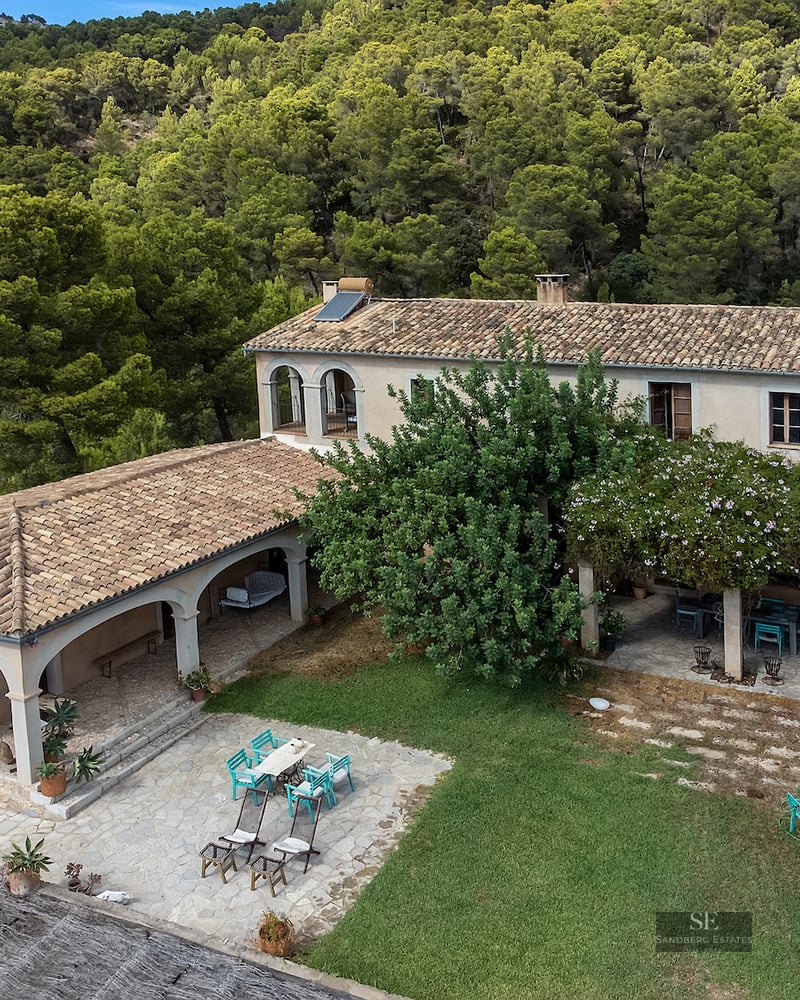 Aerial view of a traditional stone villa with terracotta roofs and arched patios surrounded by dense green forest.