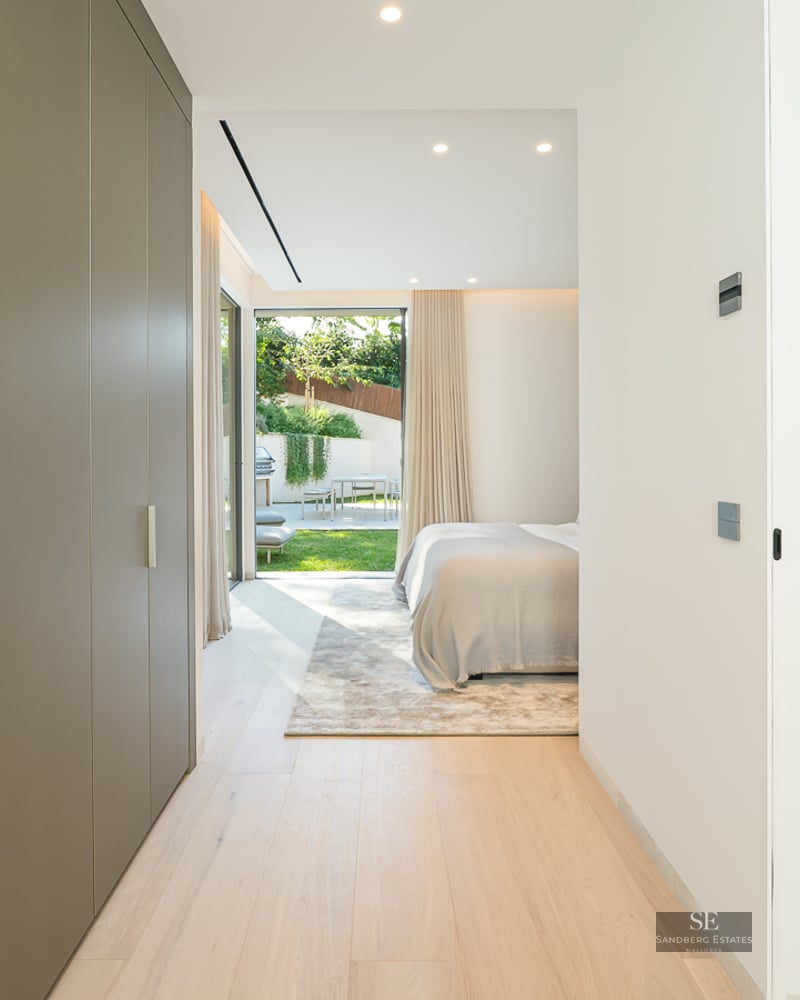 Hallway with built-in closets leading to a modern bedroom with a glass shower and view of a sunny garden.