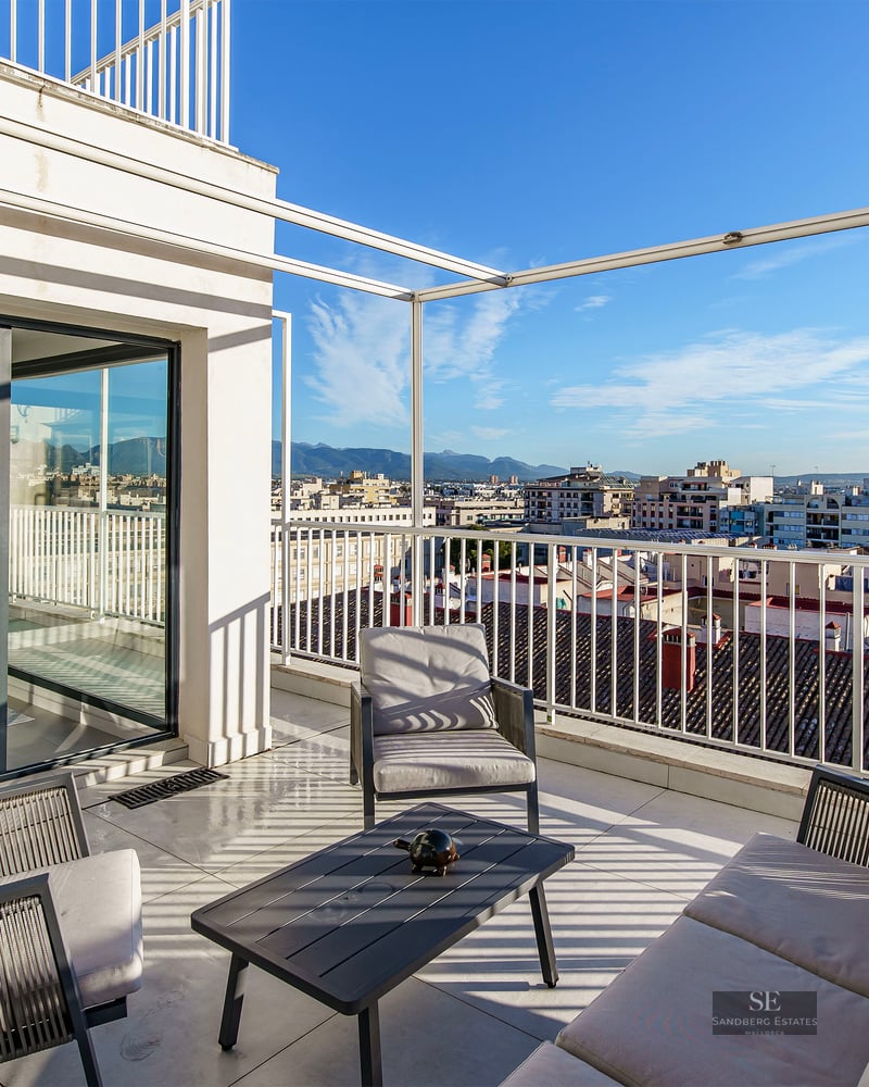 Spacious white terrace with modern outdoor lounge furniture overlooking a cityscape and distant mountains under a blue sky.