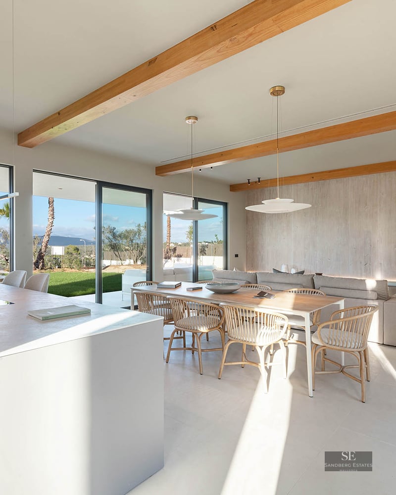 Spacious open-plan living room featuring wooden ceiling beams, kitchen island, dining area, and large glass doors to garden.