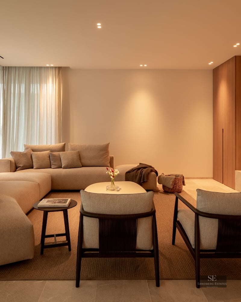 Elegant living room with large beige modular sofa, wooden wall paneling with integrated TV, and warm lighting.