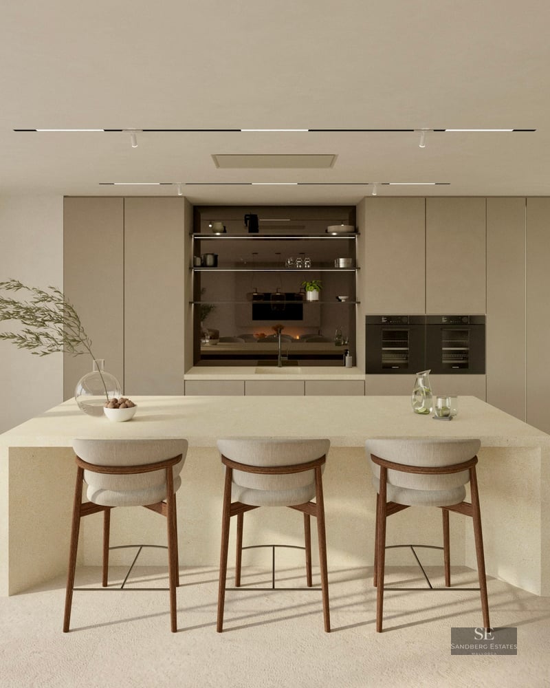 Bright minimalist kitchen featuring a large stone island with three bar stools and garden views through glass doors.