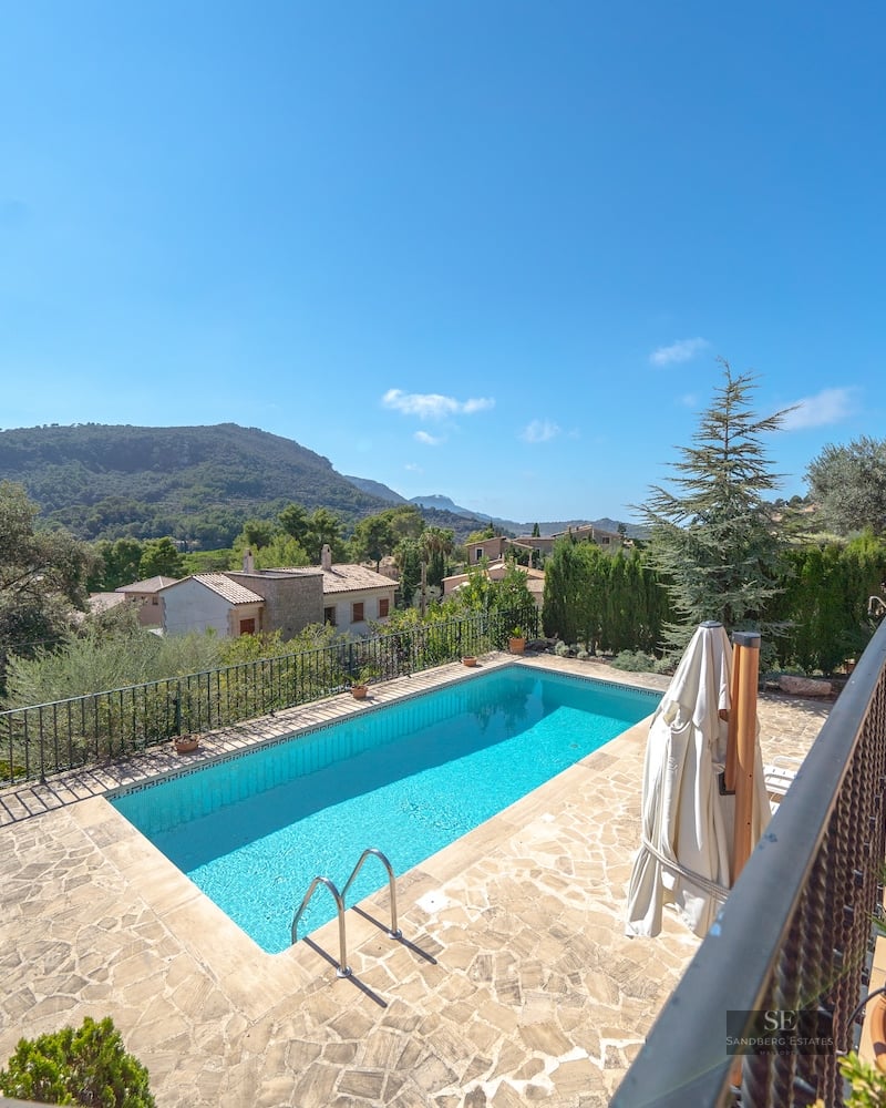 Rectangular swimming pool surrounded by a stone terrace with panoramic mountain views under a clear blue sky.