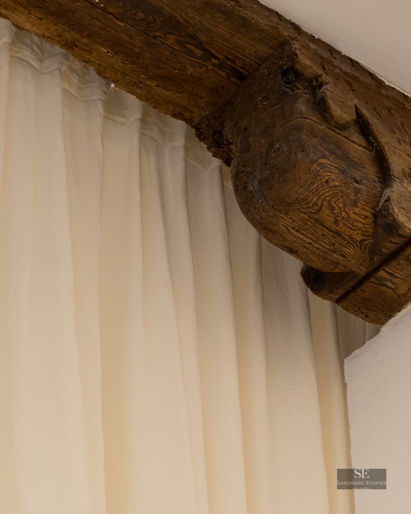 Gros plan d'un corbeau en bois sculpté à la main et d'une poutre sombre à côté de rideaux blancs fluides.