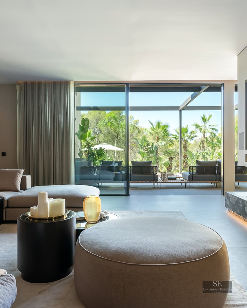 Modern living room with grey sectional sofa, linear fireplace, and floor-to-ceiling glass doors opening to a garden.