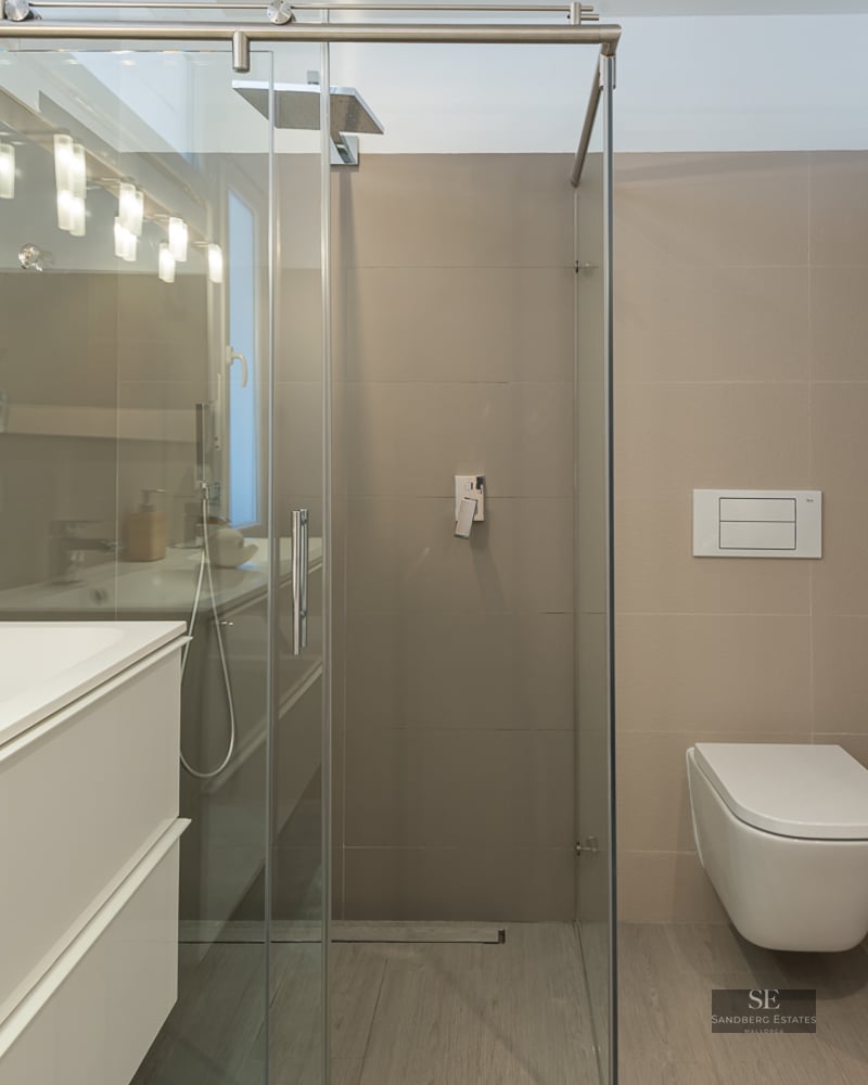 Modern bathroom featuring a white vanity, glass shower enclosure, and a wall-mounted toilet with neutral tiling.