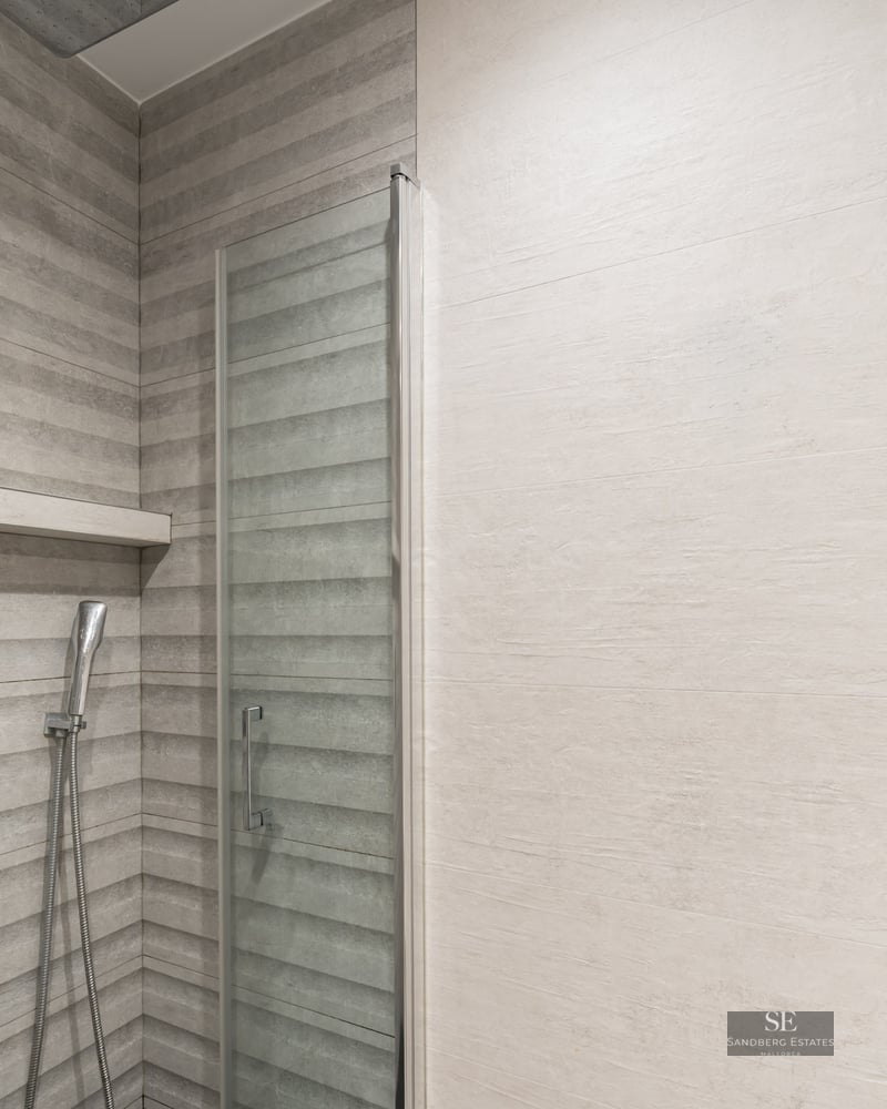 Douche moderne avec carrelage gris texturé, paroi en verre et robinetterie en chrome.