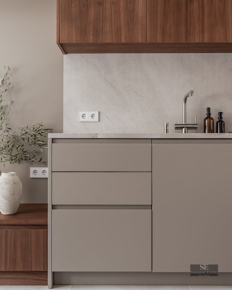 Modern kitchen with taupe cabinets, stone countertop, and walnut wood accents next to a TV unit.