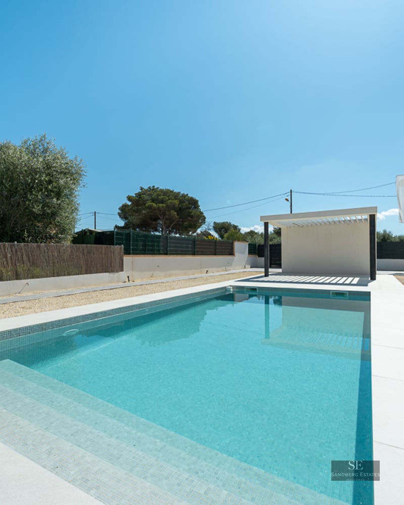 Rectangular turquoise pool with white tile border and a modern white pergola under a clear blue sky.