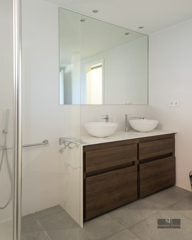 Bright modern bathroom featuring a wood double vanity with marble top, twin vessel sinks, and a glass shower.