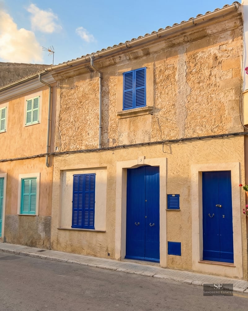 Ochre stone facade featuring vibrant blue wooden doors and shutters on a quiet street.