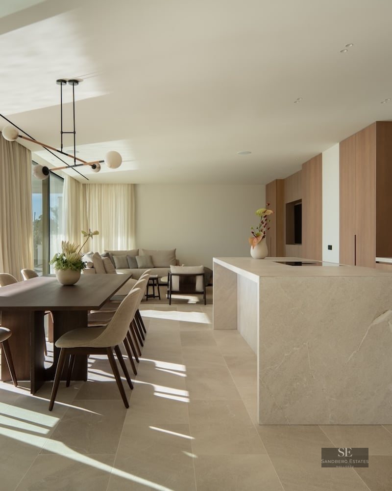 Spacious open-concept room featuring a stone kitchen island, wooden dining table, and floor-to-ceiling terrace doors.