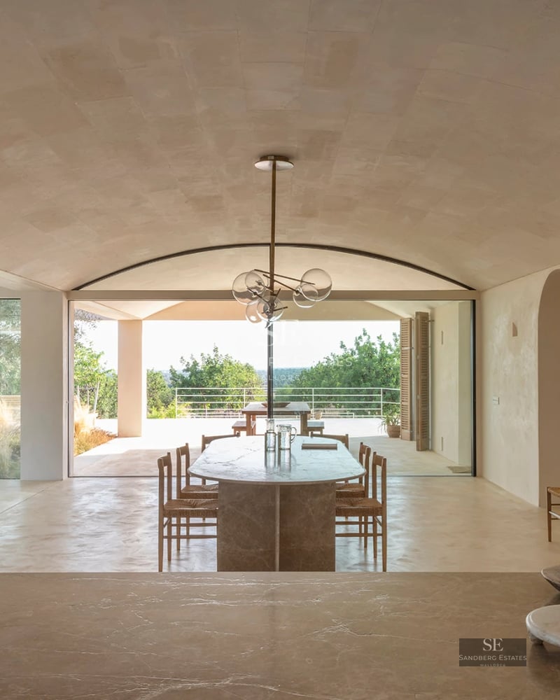 Large swimming pool with sun loungers, umbrellas, and lush greenery. Modern house in the background with large windows and a balcony.