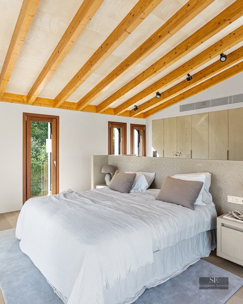 Modern master bedroom with vaulted ceiling, wooden beams, large bed, and built-in wardrobes.