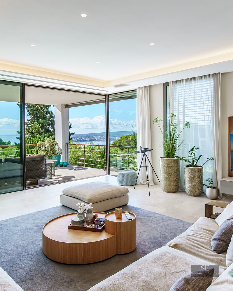 Salon moderne avec baies vitrées du sol au plafond s'ouvrant sur une terrasse avec vue sur mer.