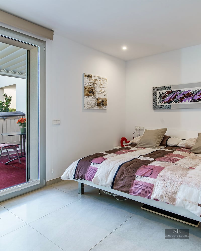 Bright bedroom featuring a double bed, modern art, and a large sliding glass door opening onto a private terrace.