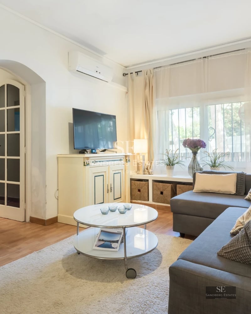 Spacious living room with floor-to-ceiling windows, light wood floors, and modern furniture. Abundant natural light. Garden view.