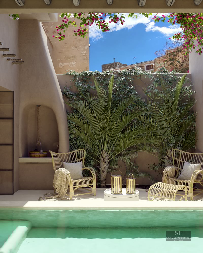 Sunlit courtyard with turquoise plunge pool, waterfall, wicker chairs, and lush greenery under a blue sky.
