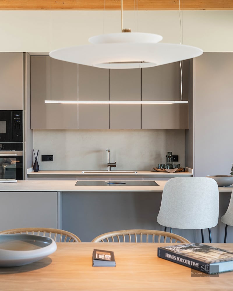 A contemporary kitchen featuring taupe handleless cabinets, a central island with stools, and elegant pendant lights.