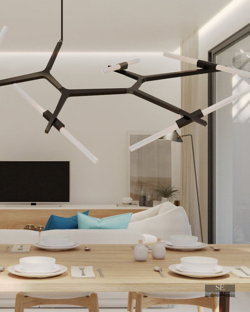 Modern dining area with a light wood table and designer chandelier, overlooking a white sofa and bright interior.