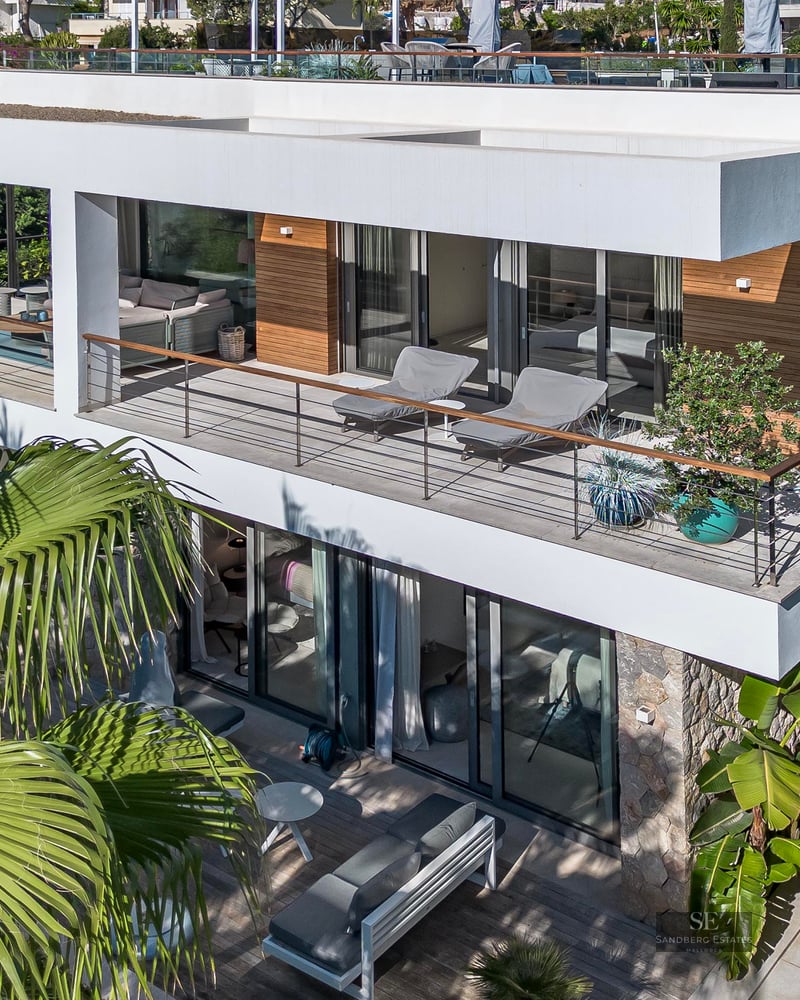 Vue aérienne d'une villa moderne blanche de deux étages avec balcons en verre et palmiers tropicaux.