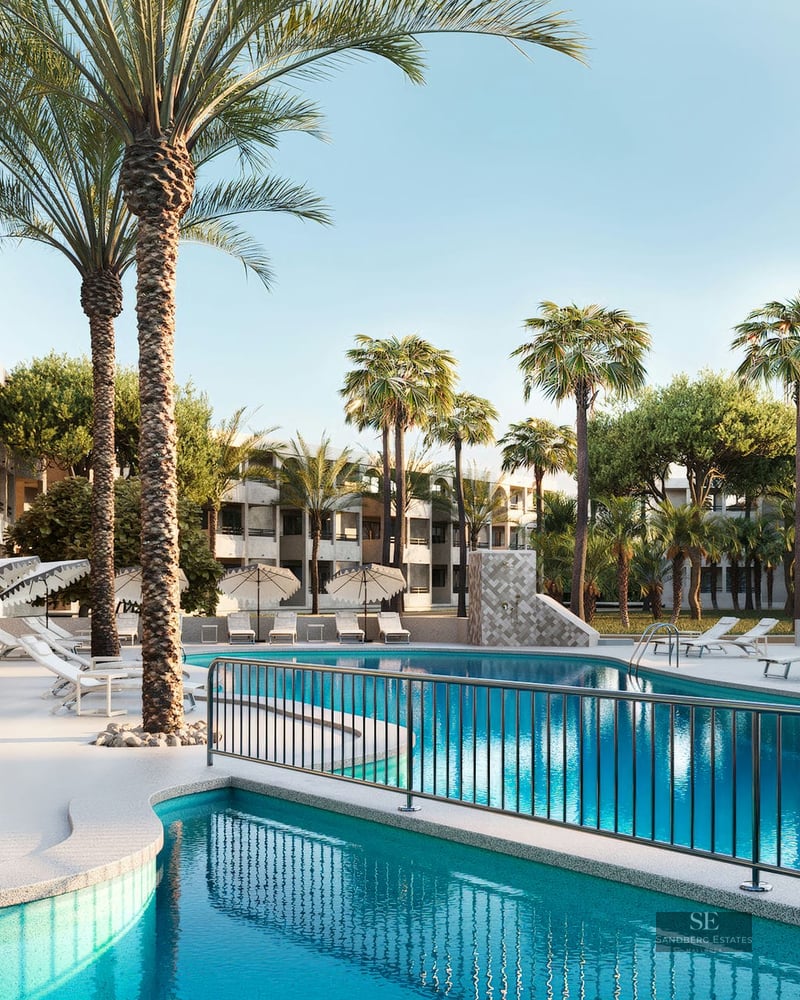 Grande piscine turquoise entourée de chaises longues blanches et de hauts palmiers devant un bâtiment moderne.