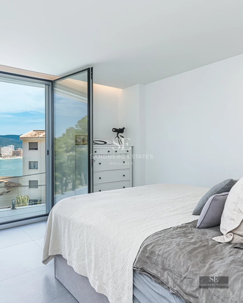 Spacious, bright living room with panoramic windows, light wood floors, and minimalist decor. Stunning sea views.