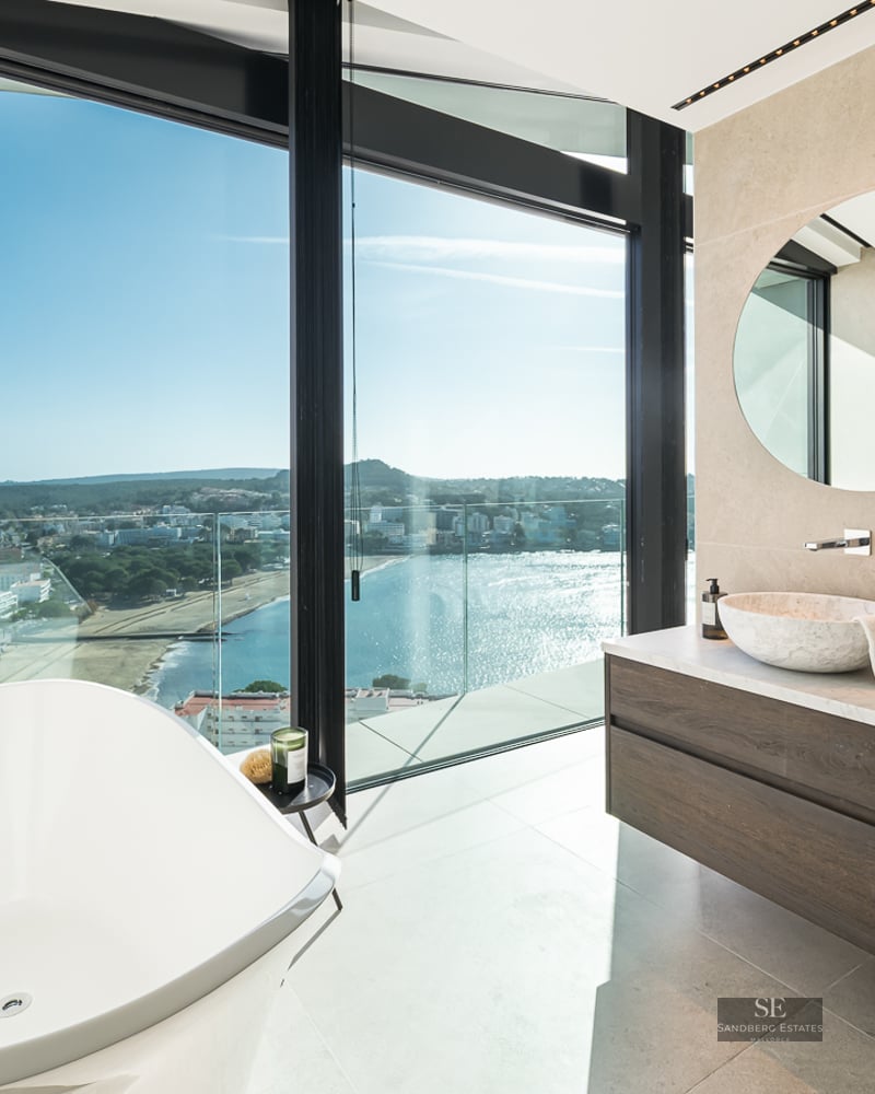 A modern bathroom featuring a white freestanding tub and large windows overlooking the ocean and coastline.