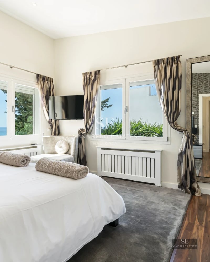 Spacious living room with floor-to-ceiling windows overlooking the sea. Modern sofa, light rug, minimalist details. Abundant natural light.