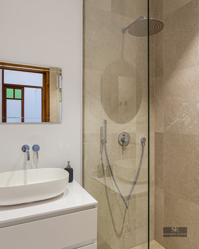 Modern bathroom featuring a white vessel sink on a white vanity and a walk-in shower with beige stone tiles.