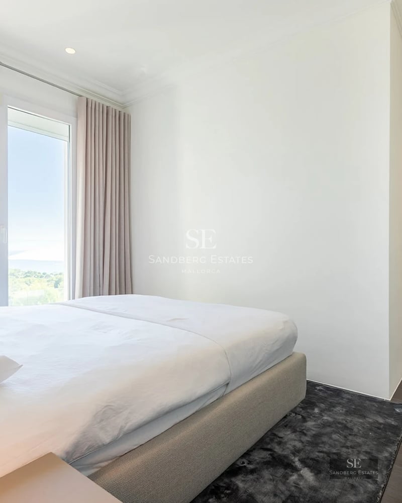 Bright bedroom with a large bed, floor-to-ceiling windows, and elegant neutral-toned curtains.