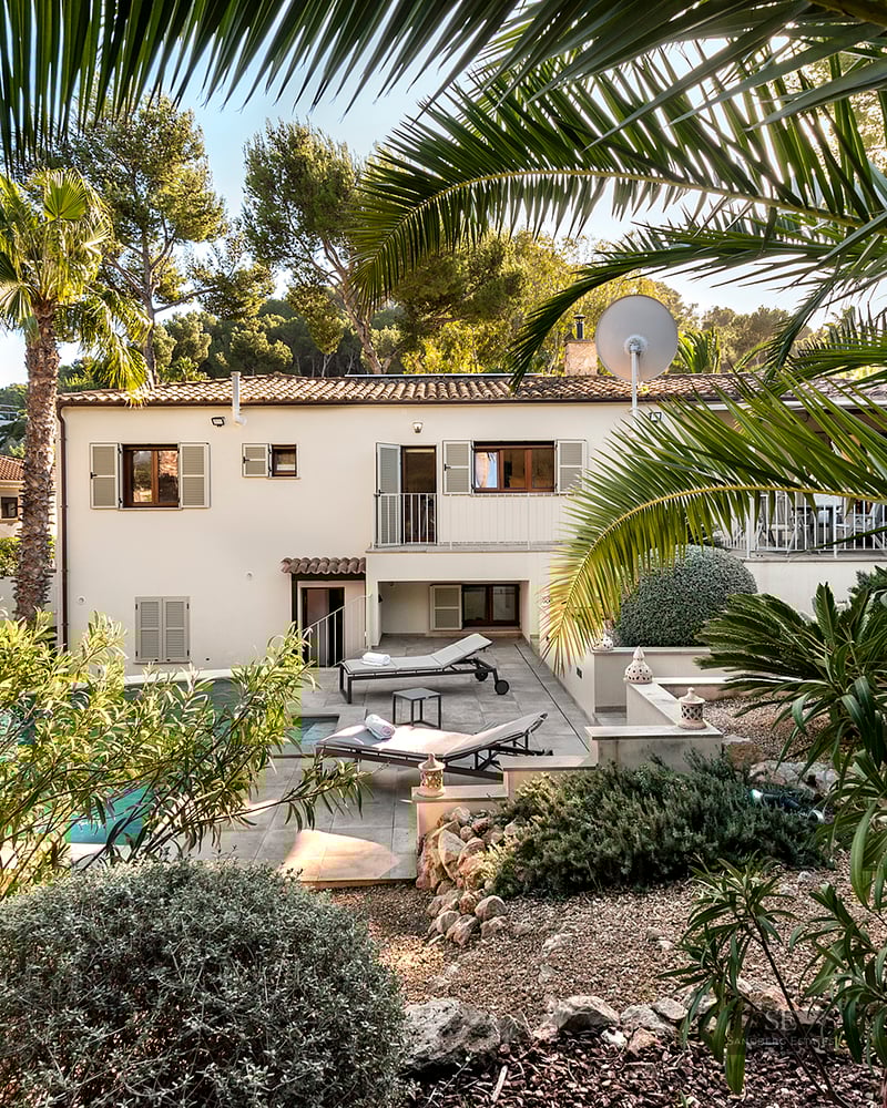 Two-story villa with a private swimming pool, sun loungers, and lush Mediterranean greenery under a clear sky.