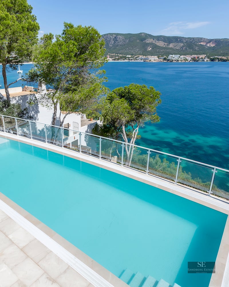 An elevated view of a turquoise infinity pool overlooking the Mediterranean sea with mountains in the background.