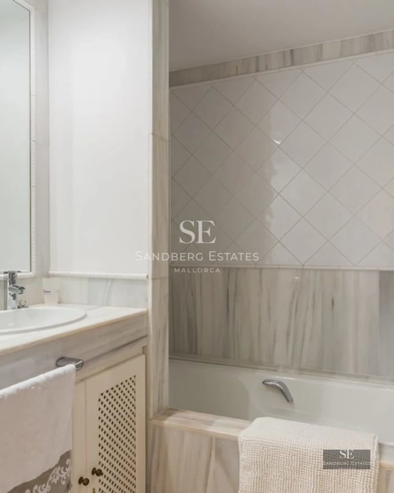 View of a luxurious pool with sun loungers, lush greenery, and a modern house with large windows in the background.