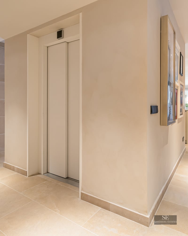 Spacious modern home entrance featuring a private elevator, beige stone floors, and a view into a bright living room.