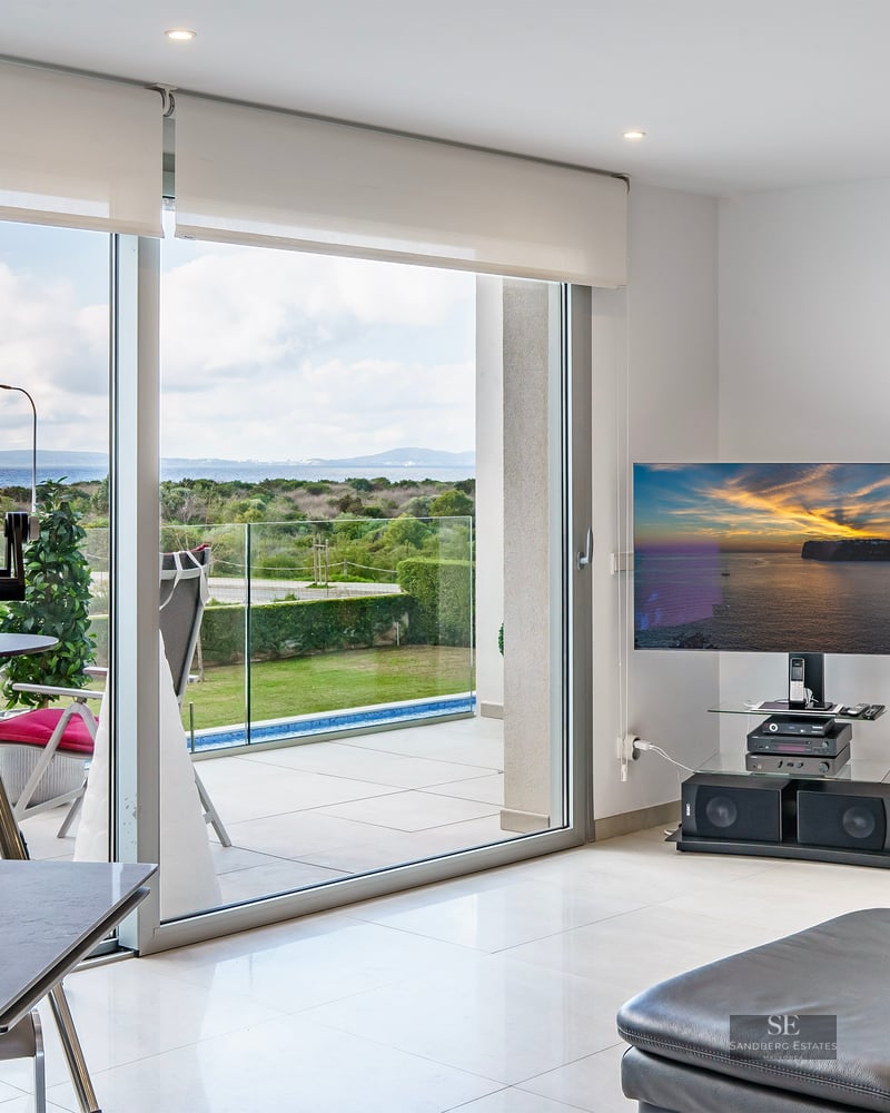 Bright living room with large glass doors opening to a terrace with sea views, featuring a TV and leather sofa.