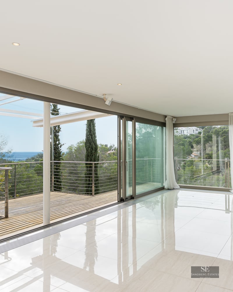 Bright, empty modern living room with polished floors and glass sliding doors opening to a terrace with sea views.