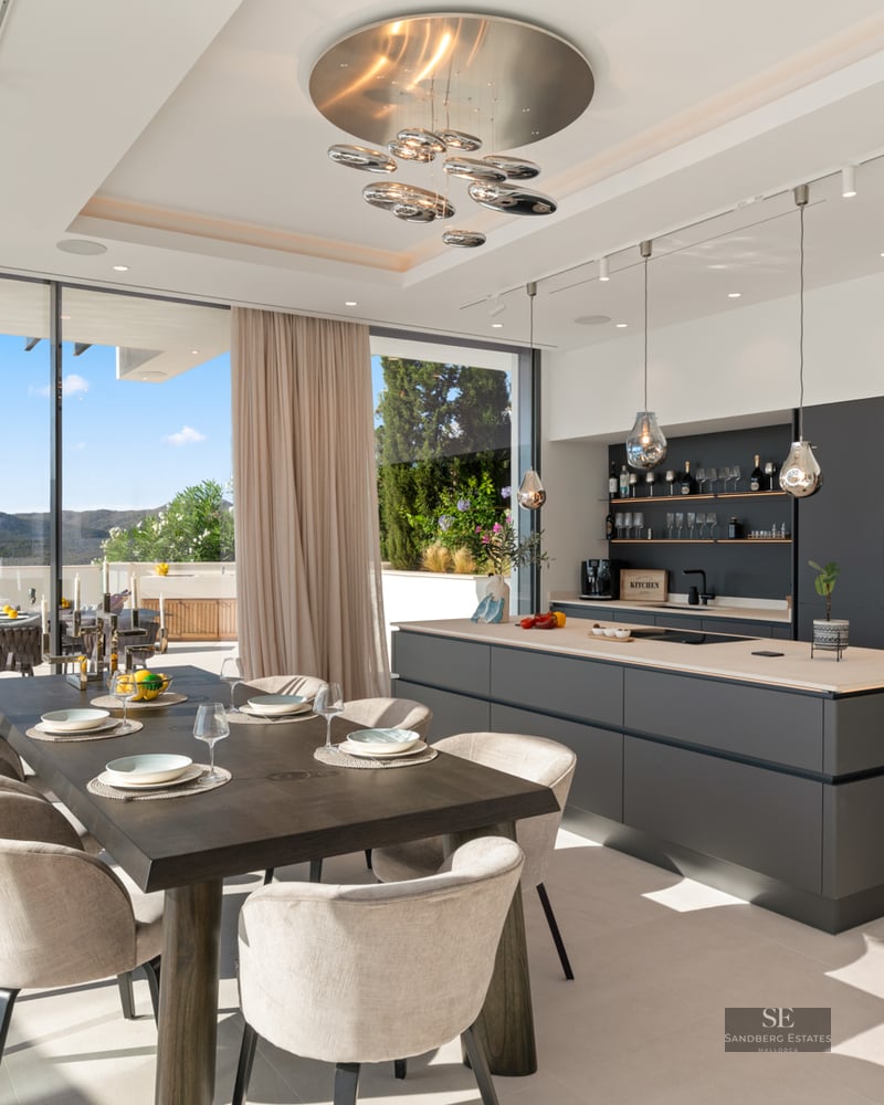 Modern kitchen with large grey island and wooden dining table next to floor-to-ceiling windows with mountain views.