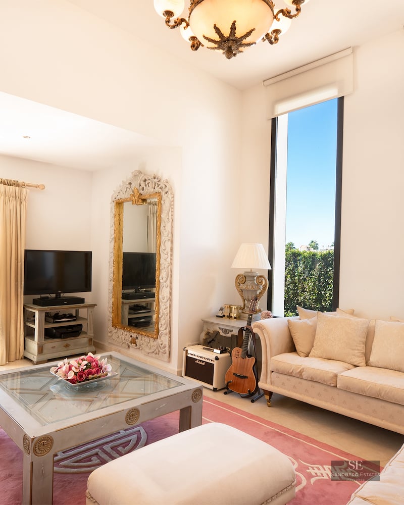 Bright living room with cream sofas, a pink rug, large vertical windows, and a sliding door leading to a balcony.