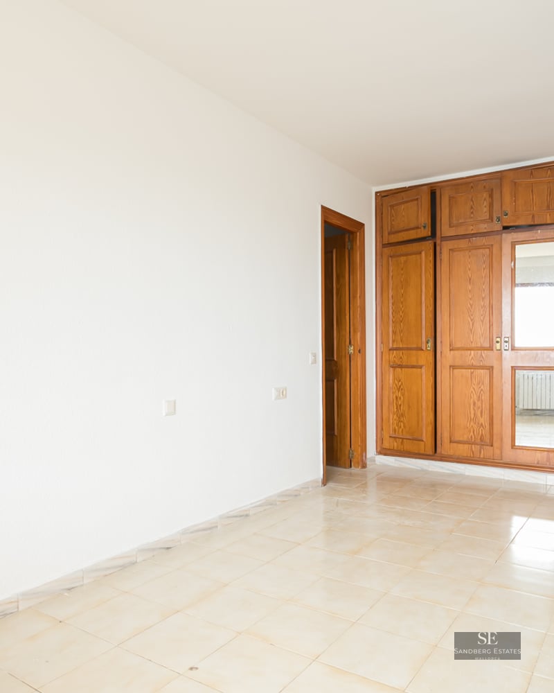 Empty room with white walls, beige tiled floor, and a large built-in wooden wardrobe with a mirrored panel.