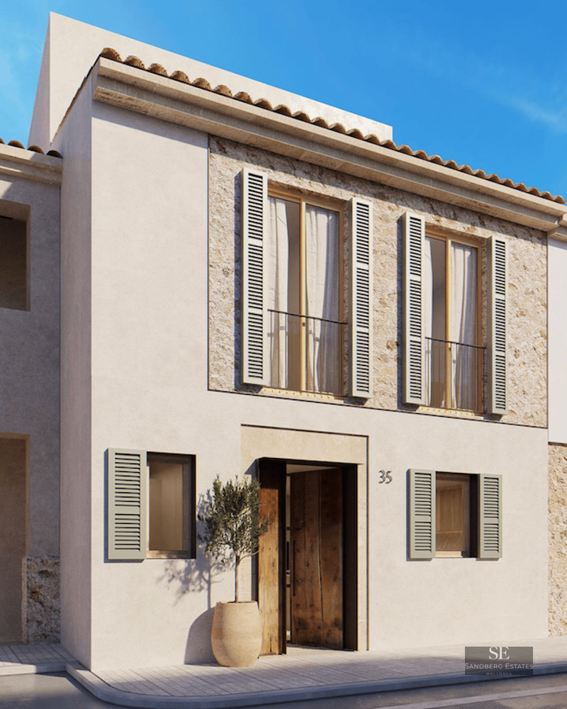 Beige stucco building with sage green shutters, natural stone accents, and a wooden door under a clear blue sky.
