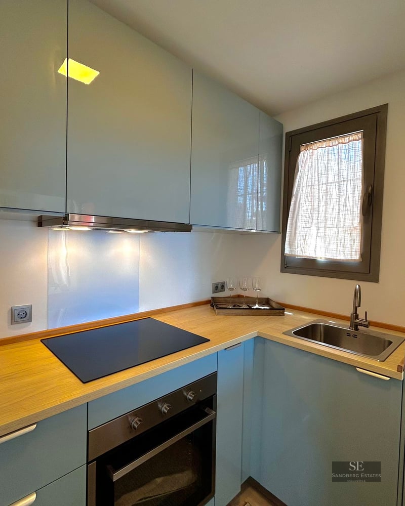 Modern kitchen featuring glossy light blue cabinets, light wood countertops, induction hob, and stainless steel sink.
