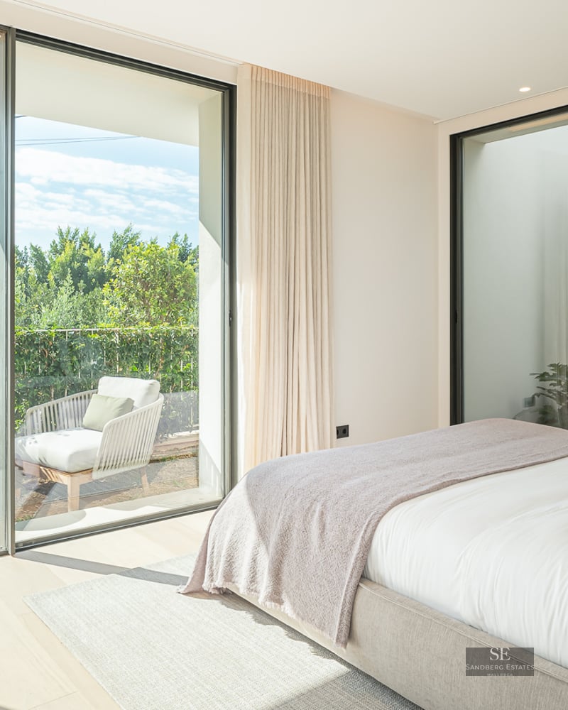 Bright master bedroom featuring floor-to-ceiling glass doors opening onto a private terrace with lush greenery.