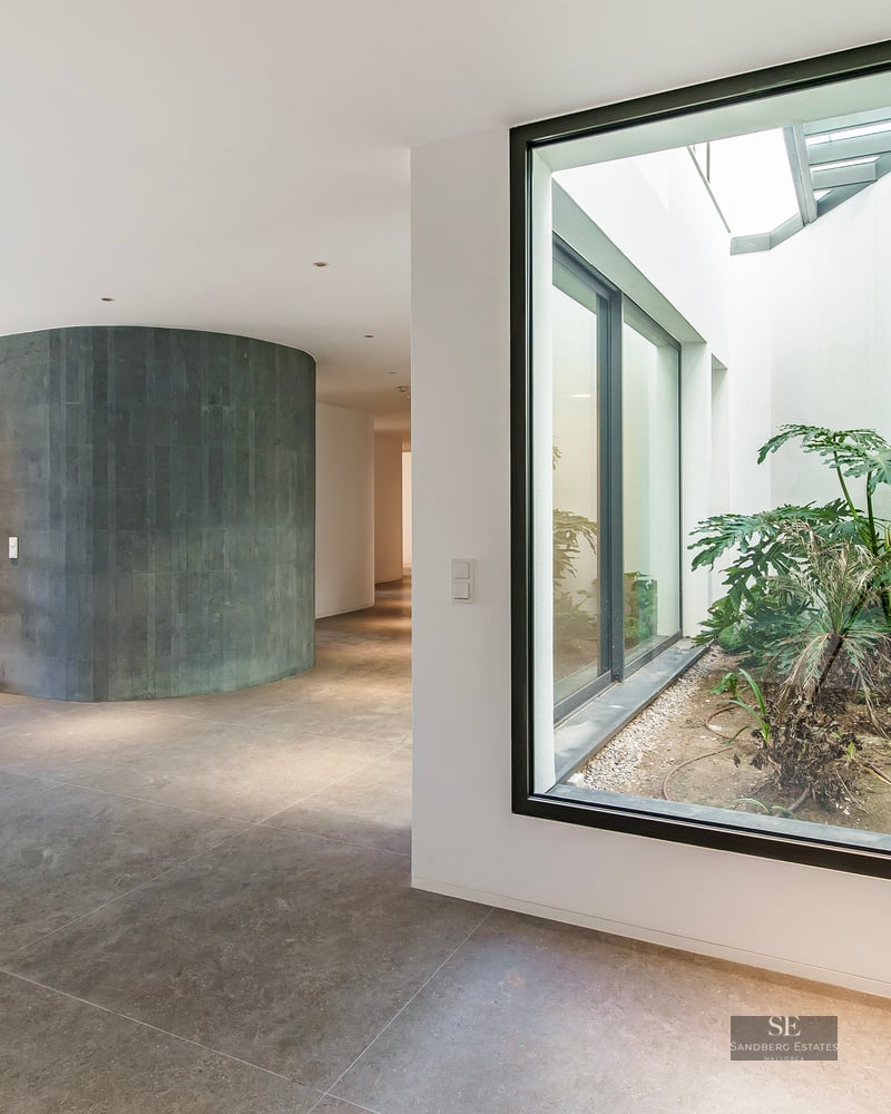 Modern hallway featuring a curved grey stone wall and a large glass window looking onto an interior garden patio.