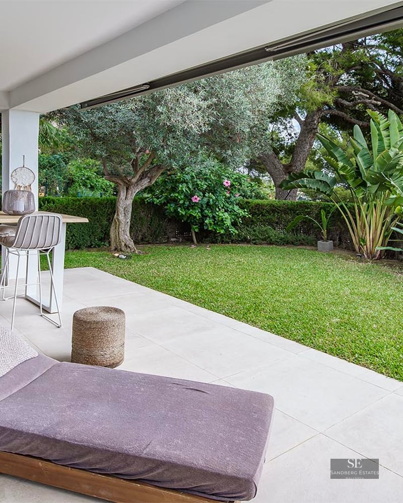 Covered terrace with dining table, sun lounger, and manicured green garden with partial sea views.
