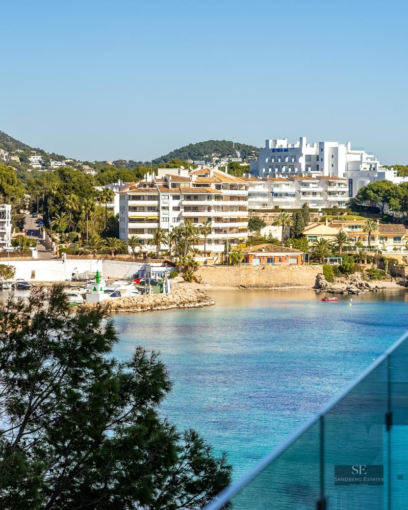 High-angle view of a turquoise bay with white buildings and a marina seen through a glass balcony railing.